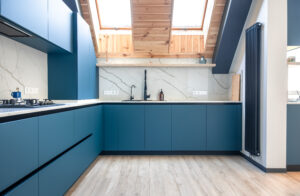 Corner attic kitchen with matte blue cabinets, light wood accents, and Scandinavian aesthetic. Bright, ergonomic and stylish cooking area with natural light.